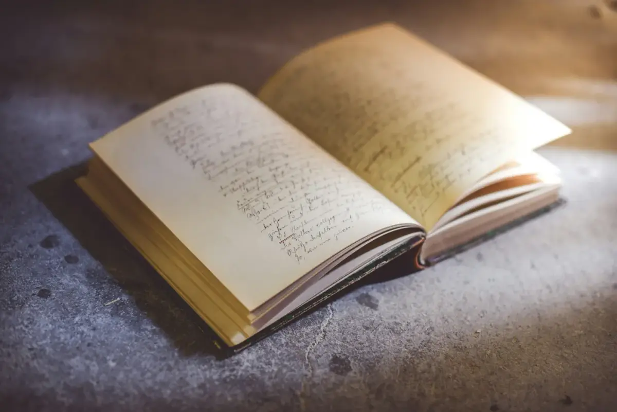 An open notebook of handwritten pages lying on a stone surface in warm light.