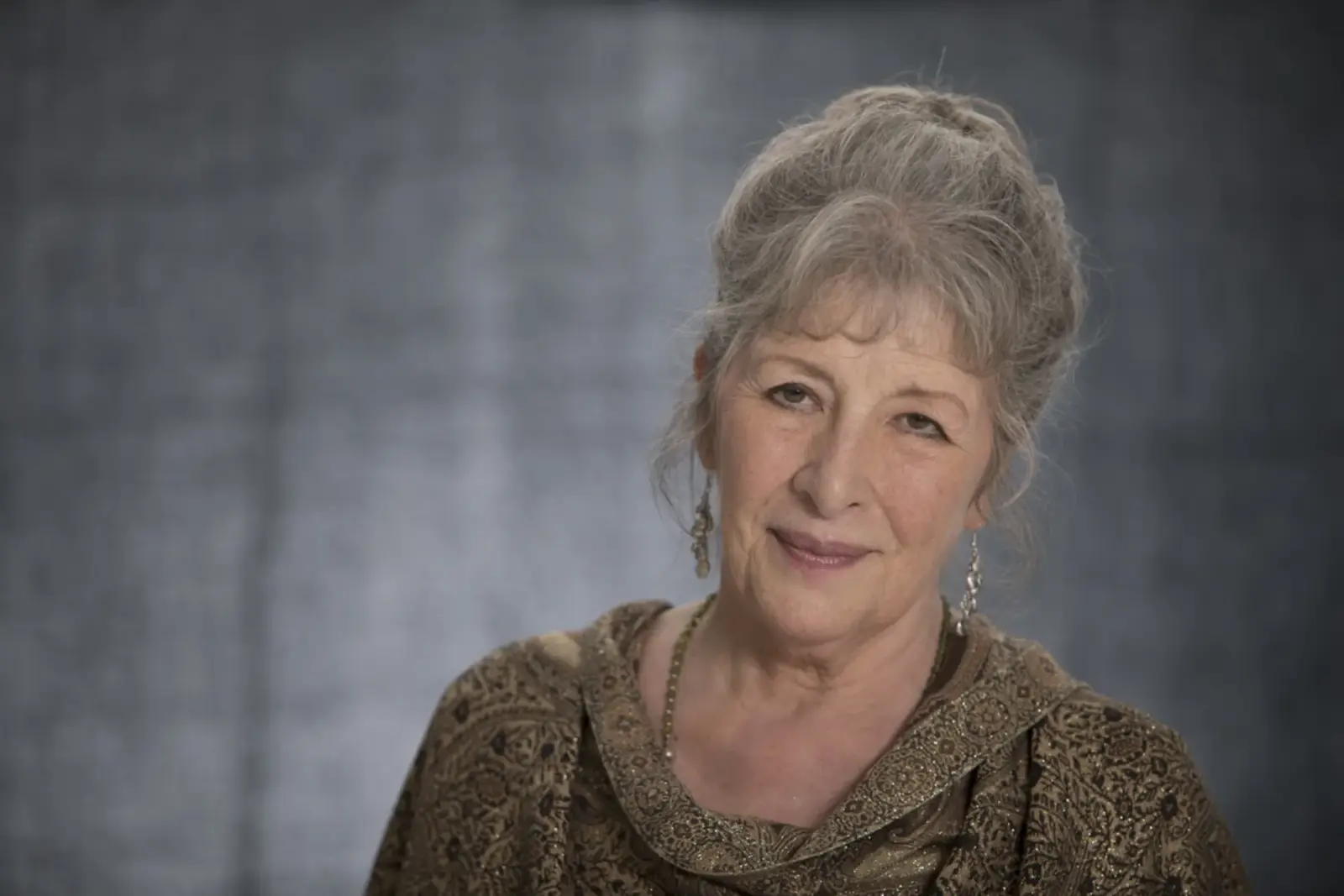 Maxine Sanders, smiling, with her silver hair pinned up and long earrings.