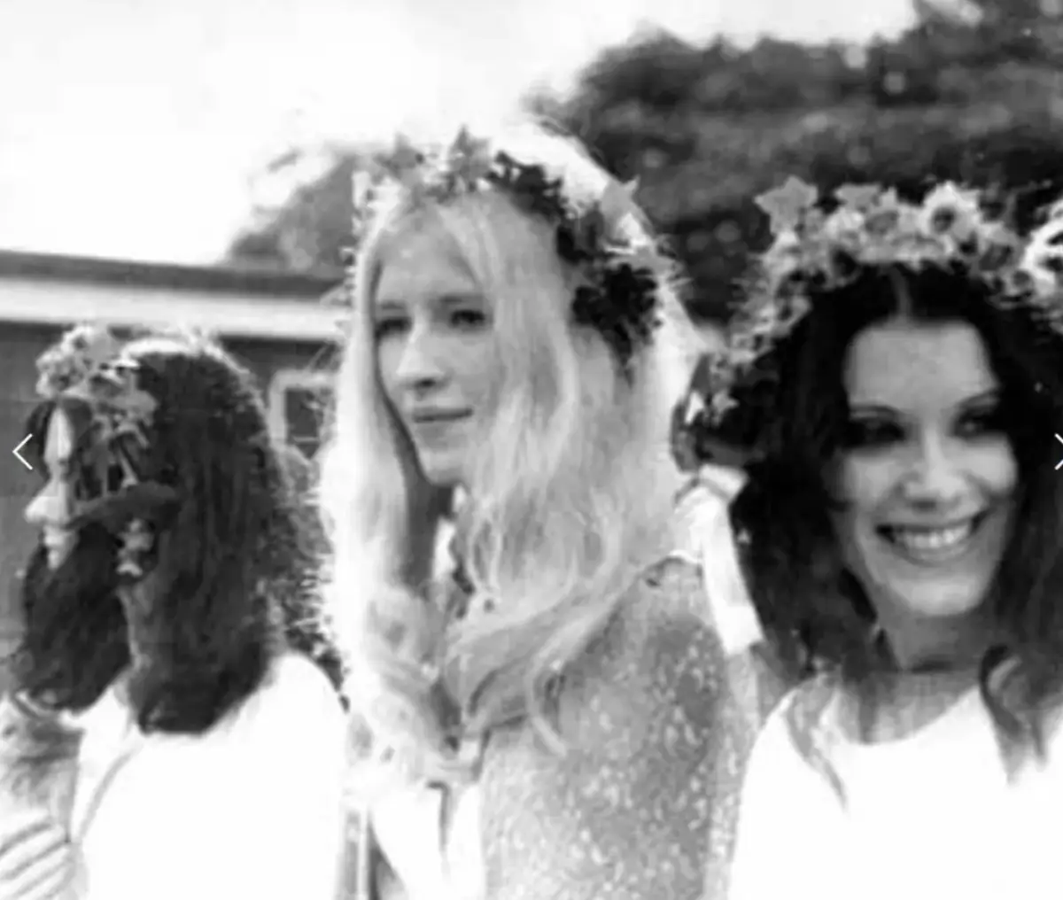 A black-and-white photograph of three young women in flower crowns at an outdoor ceremony, Maxine fair-haired in the middle.